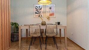 Een eetruimte met een houten tafel, twee rieten stoelen, een hanglamp en twee ingelijste abstracte kunstwerken aan de muur.