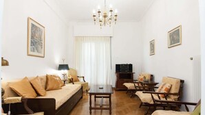 Een gemeubileerde woonkamer met een bank, stoelen, een tafel, een televisie en kunstwerken aan de muren.