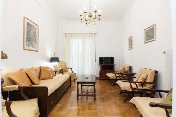 A furnished living room with a sofa, chairs, a table, a TV, and artwork on the walls.