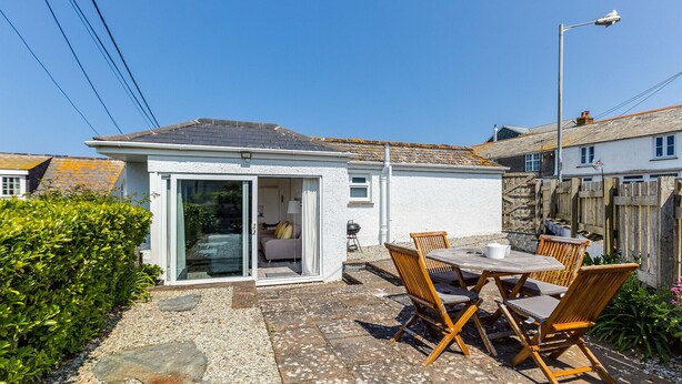 A small house with a patio, a sliding glass door leading to a bedroom, and a table with chairs.