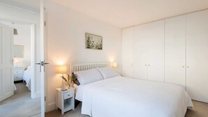 A bedroom with a bed, bedside tables, a nightstand, a door, and a wardrobe.