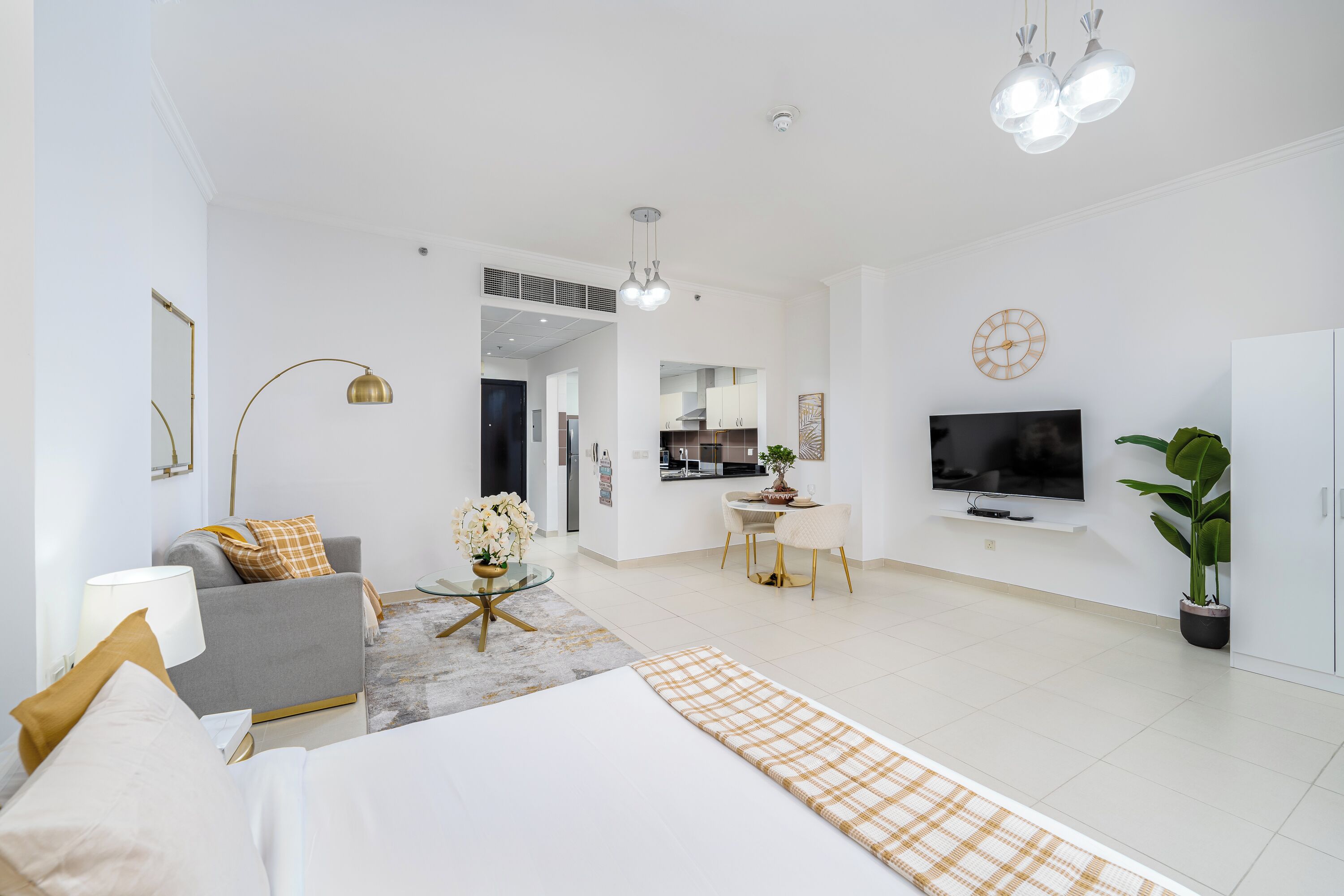 A modern hotel room with a bed, a sofa, a dining area, a TV, and a plant.