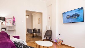 A modern living room with a purple sofa, a white coffee table, and a dining area with chairs and a table. - Sleek & Modern Apartment Near Metaxourgeio (Athens)
