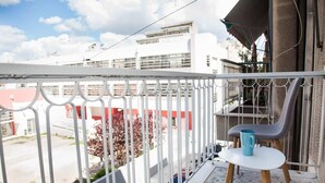 A balcony with a white railing, a small table with a blue mug, and a view of buildings and trees. - Sleek & Modern Apartment Near Metaxourgeio (Athens)