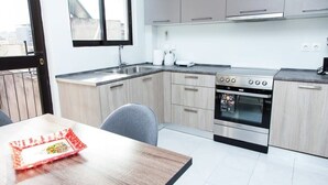 A modern kitchen with light wood cabinets, a stainless steel stove, and a dining area with a wooden table and chairs. - Modern apt in heart of Paleo Faliro! (Athens)