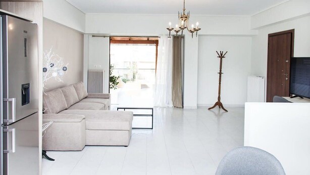 A modern living room with a sofa, a dining table, and a television. - Modern apt in heart of Paleo Faliro! (Athens)