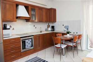 Een moderne keuken met houten kastjes, een inbouwoven, een koffiezetapparaat en een eethoek met stoelen.