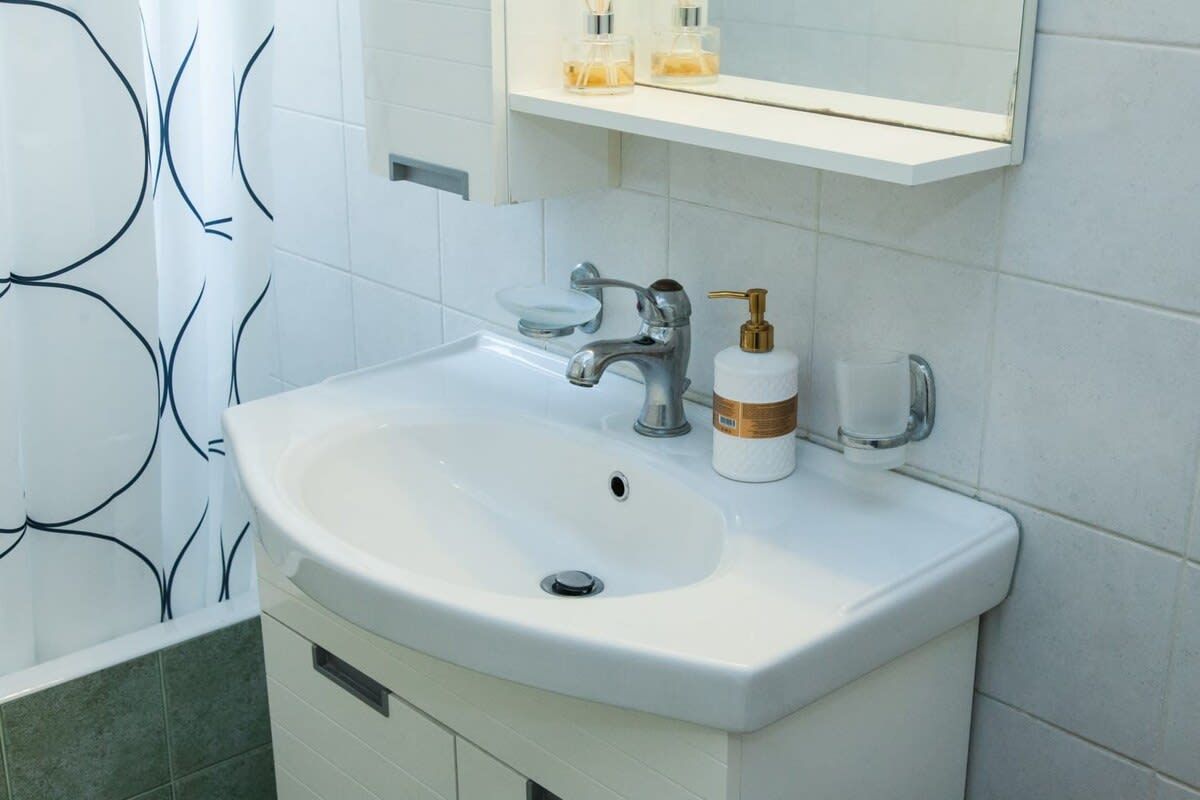 Une salle de bain avec un lavabo blanc, un miroir au-dessus, et un rideau de douche à motifs noirs et blancs.