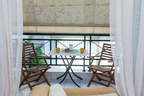 A balcony with a table and two chairs, a view of greenery, and a patterned ceiling. - Cozy modern apt in Peristeri (Athens)