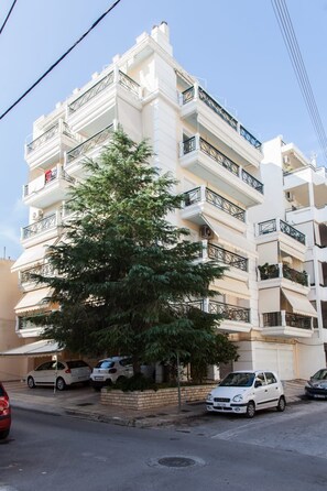 A multi-story residential building with balconies, parked cars, and a tree in front. - Cozy modern apt in Peristeri (Athens)