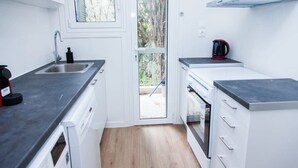 Une cuisine de taille réduite avec des meubles blancs, un plan de travail noir, un évier en acier inoxydable et une bouilloire rouge.