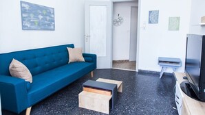 A modern living room with a blue sofa, a small wooden coffee table, a TV on a wooden stand, and a door leading to another room. - Piraeus 1 Bd Cosy Apt with Balcony (Athens)