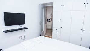 A bedroom with a bed, a TV mounted on the wall, a wardrobe, and a door leading to another room. - Piraeus 1 Bd Cosy Apt with Balcony (Athens)