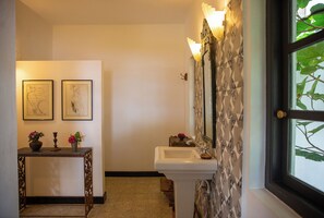 A bathroom with a sink, mirror, and window. There are two framed artworks on the wall and a small table with a vase and candle. - Isla's Ridge (Athur)