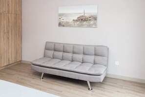 A grey sofa with a cushioned backrest and metal legs, positioned in a room with a wooden floor and a white wall. - Modern Luxury Central Acropolis View Penthouse (Athens)