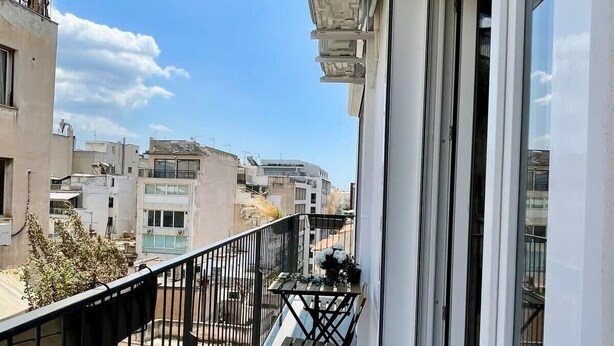 Ein Balkon mit Blick auf benachbarte Gebäude, einem kleinen Tisch mit Stühlen und einem Blumentopf.