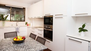A modern kitchen with white cabinets, a granite countertop, and a dining area with a table set for four. - Delux Apartment with Amazing Balcony! (Athens)