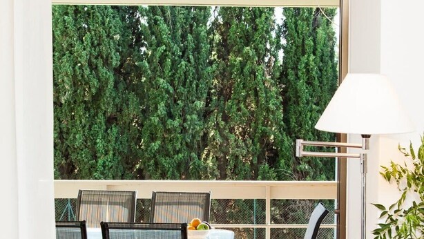 A modern room with a wooden floor, a dining table with chairs, a floor lamp, and a view of greenery outside. - Delux Apartment with Amazing Balcony! (Athens)