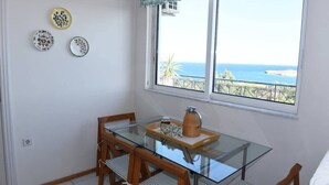 A dining area with a glass table, wooden chairs, and a view of the sea through a window. - Top floor 3bed 2bath with stunning 360 view (Athens)