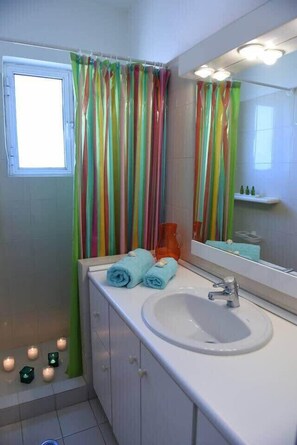Une salle de bain avec un lavabo blanc, un miroir et une fenêtre avec un rideau.