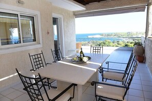 Un coin repas avec une table et des chaises, une bouteille de vin et une vue sur la mer.