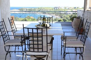 A balcony with a table set for two, overlooking a scenic view of the sea and landscape.