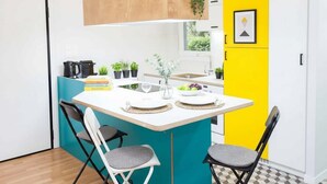A compact kitchen with a white countertop, two chairs, a small island with a vase, and a yellow accent wall.