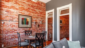 A dining area with a brick wall, a framed abstract painting, and a dining table with chairs. - Gateway Inn: Cora's Loft (Stratford)