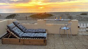 Eine Sitzecke mit gepolstertem Sofa und einem Sessel, mit Blick auf einen Strand mit Holzzaun und einem Tisch, gedeckt mit Getränken und Snacks.