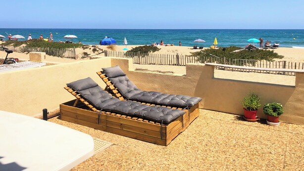 Ein Strandloungebereich mit einer Holzbank und einem weißen Tisch mit Blick aufs Meer.