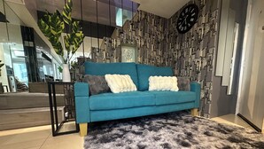 En moderne stue med en tealgrøn sofa, en stor, lodden måtte og en væg med mønster.