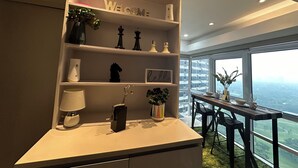 Et moderne værelse med et stort vindue, der giver udsigt over byen, et hvidt konsolbord med lampe, skakbrikker og dekorative genstande.