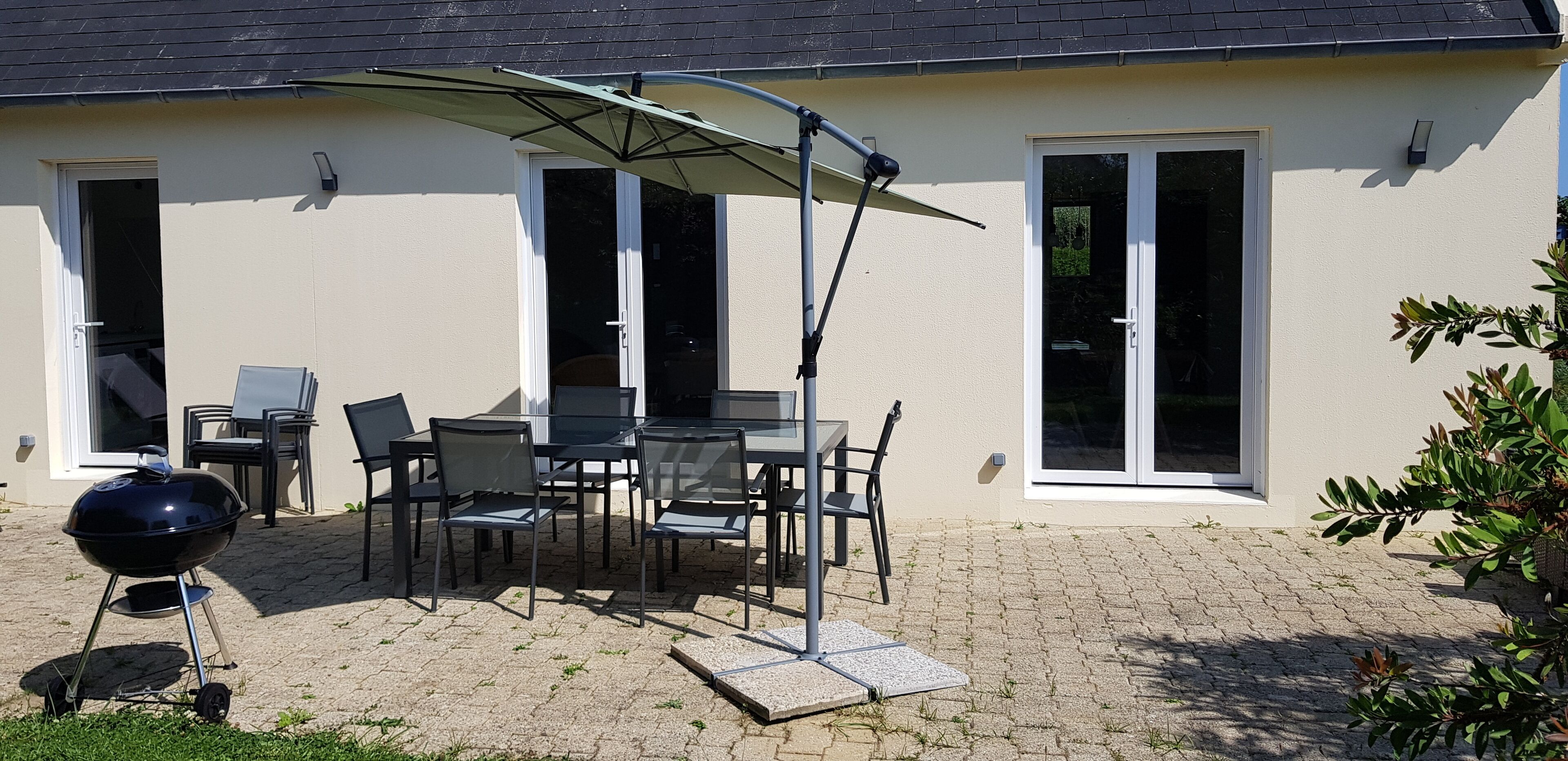 An outdoor patio with a table and chairs, a barbecue grill, and a covered umbrella.