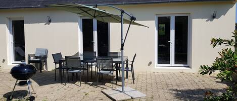 An outdoor patio with a table and chairs, a barbecue grill, and a covered umbrella.