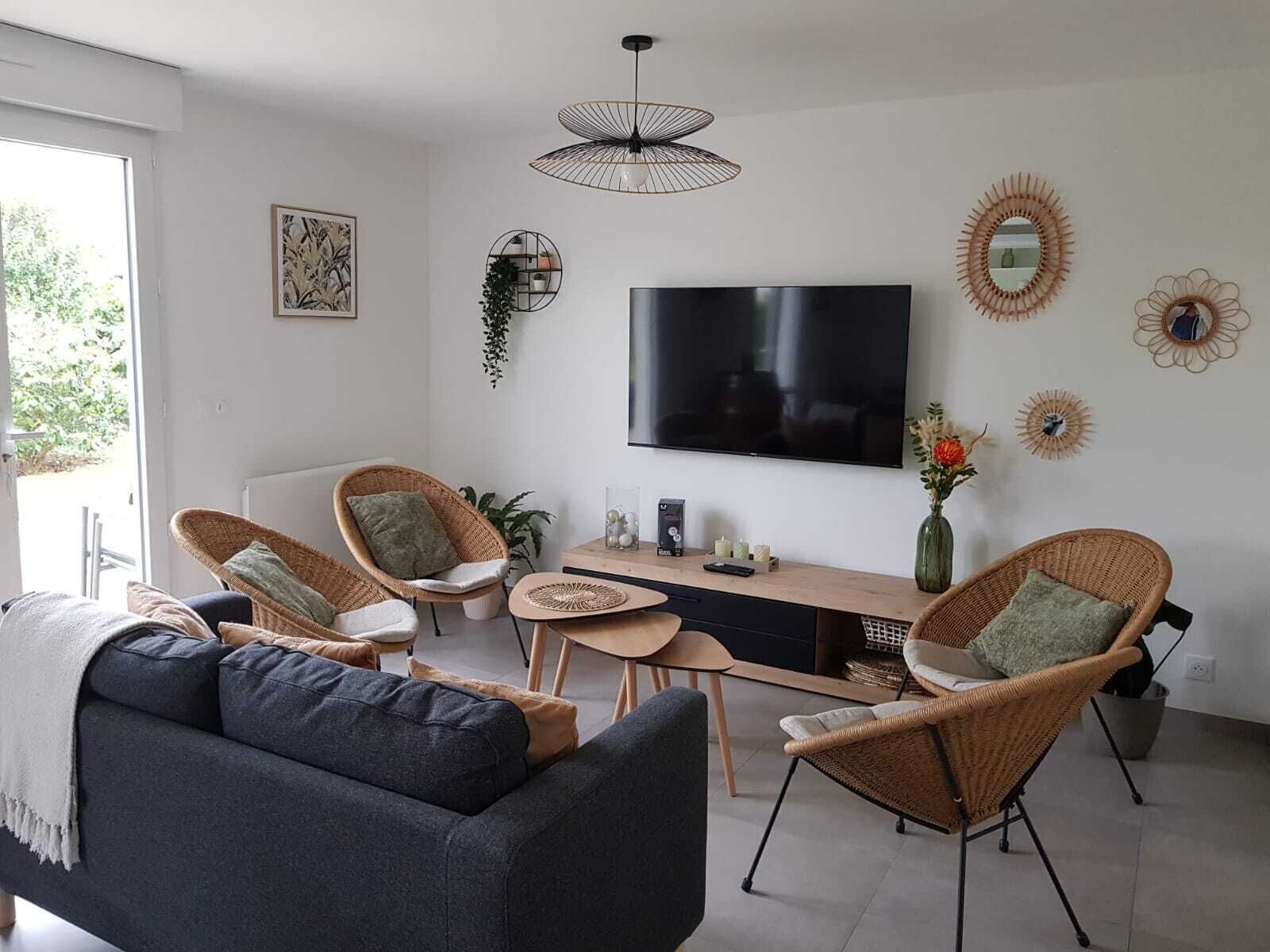 A modern living room with a sofa, two wicker chairs, a coffee table, a TV, and decorative wall art.