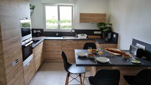A modern kitchen with wooden cabinets, a built-in oven, a dining table with chairs, and a window providing natural light. - New : House, fully renovated, with garden, 200m from the beach - 3*** French property (Loctudy)