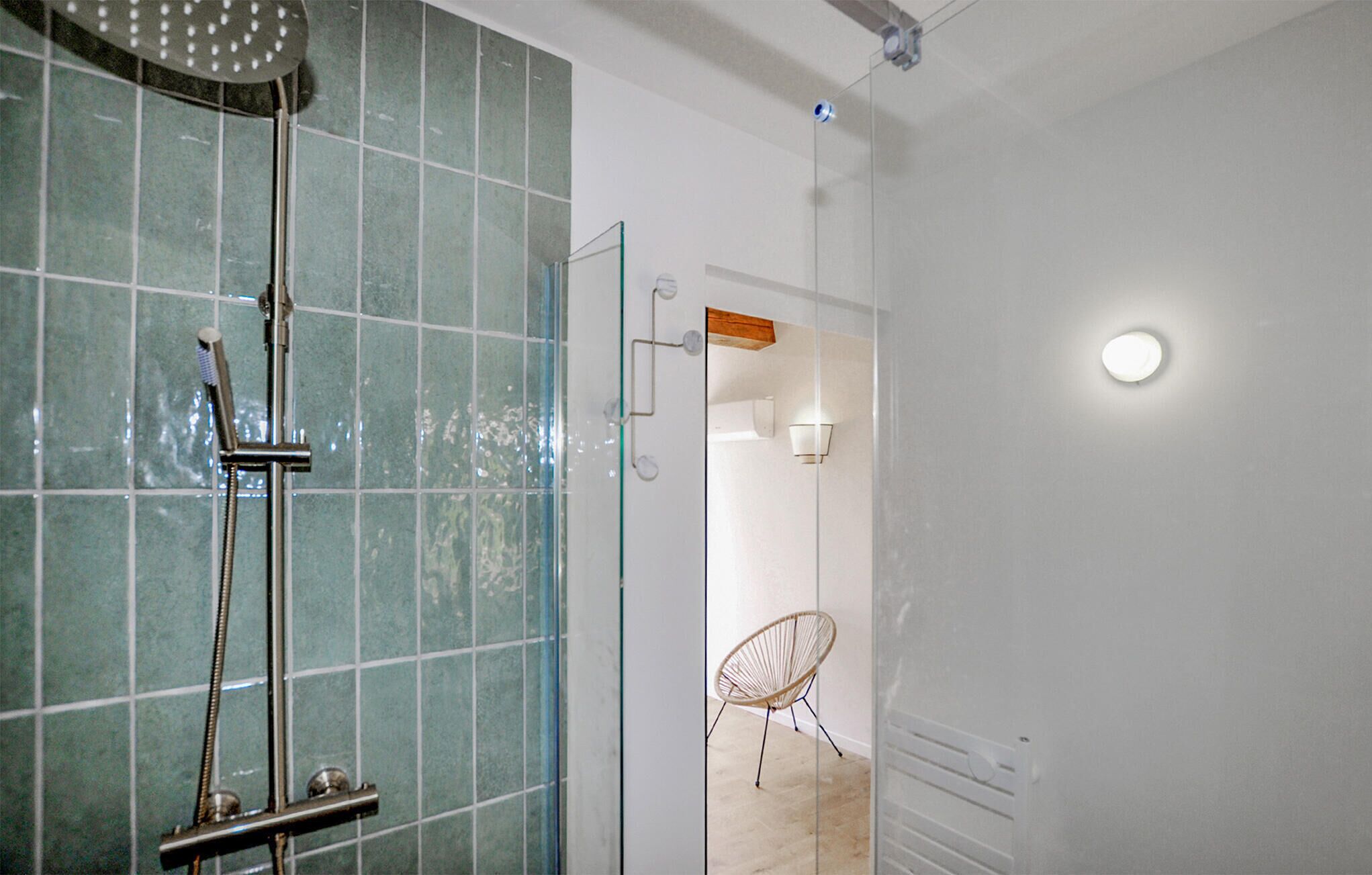 Une salle de bain avec une douche à parois de verre, une chaise blanche et une étagère en bois.