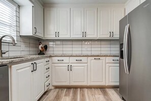 A kitchen with white cabinets, a stainless steel refrigerator, and a tiled backsplash.