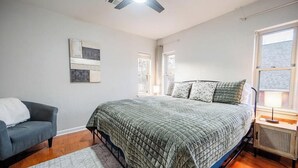 Un dormitorio con cama, una silla, un radiador y un ventilador de techo.
