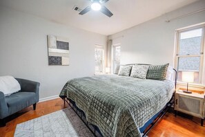 A bedroom with a bed, a chair, a radiator, and a ceiling fan.