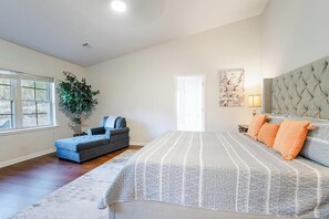 A bedroom with a large bed, a sofa, a potted plant, and a door.