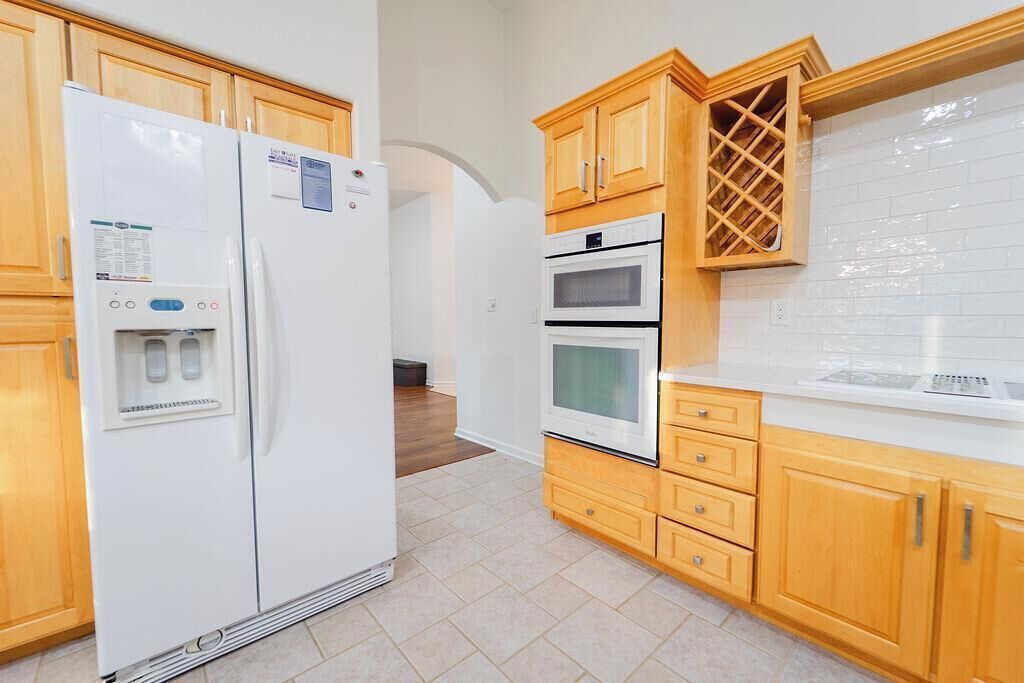 Una cocina con armarios de madera, un refrigerador blanco, un horno y una cava de vinos.