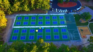 Vista aérea de un complejo deportivo con varias canchas de tenis, una cancha de baloncesto y un estacionamiento.