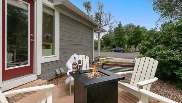 En terrasse med et sort ildstedebord, hvide Adirondack-stole og en rød dør.