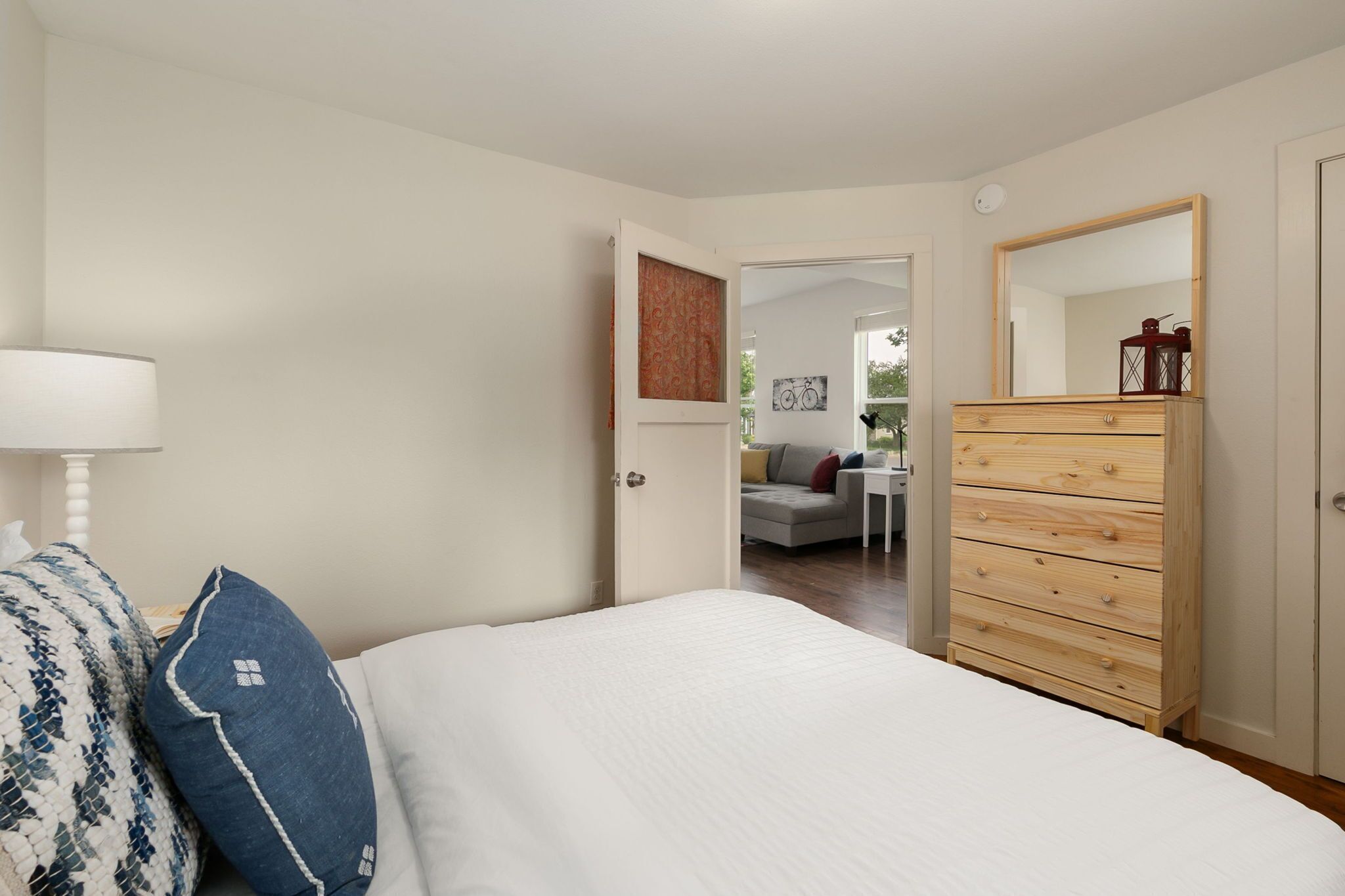 A bedroom with a bed, a dresser, a mirror, and a door leading to a living area.