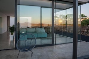 A modern living room with a glass wall, a teal sofa, and a black chair.
