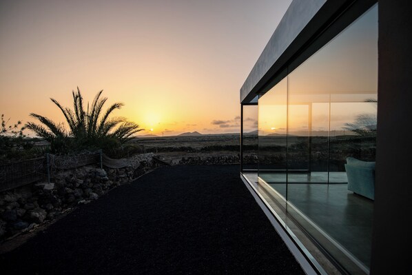 A modern building with a glass facade overlooking a desert landscape at sunset.