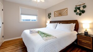 Un lit bien fait, avec du linge de lit blanc, une tête de lit en bois, une lampe de chevet et une plante fixée au mur.