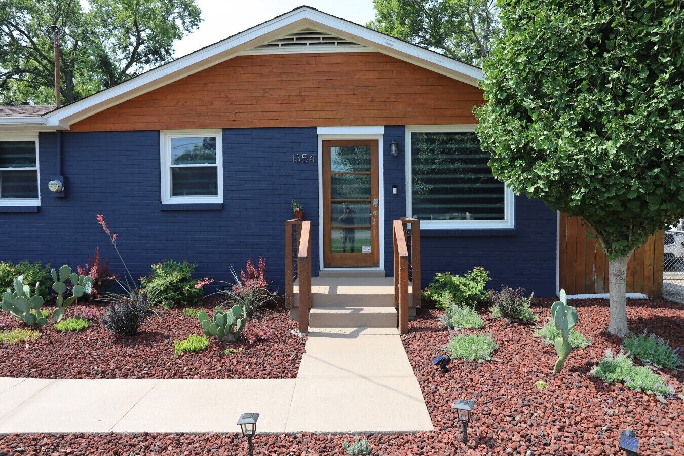 A modern two-story house with a dark blue exterior, a wooden front door, and a number '1354' on the door.