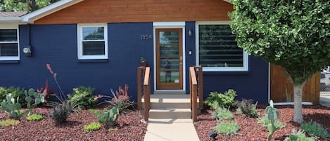 A modern two-story house with a dark blue exterior, a wooden front door, and a number '1354' on the door.